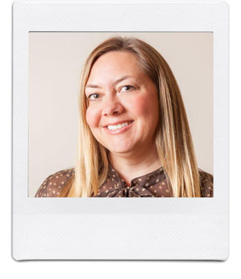 A smiling woman with long, straight blonde hair wearing a brown blouse with white polka dots. She is posed against a plain beige background, captured in a square, Polaroid-style photograph.