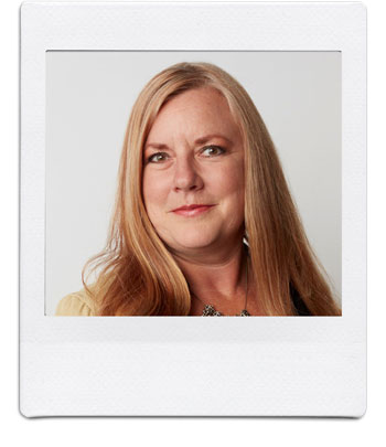 A woman with long, straight, blonde hair, wearing a beige top and a necklace, is posing for a portrait against a plain white background. She has a serious expression and a slight smile. The photo is framed to resemble a Polaroid picture.