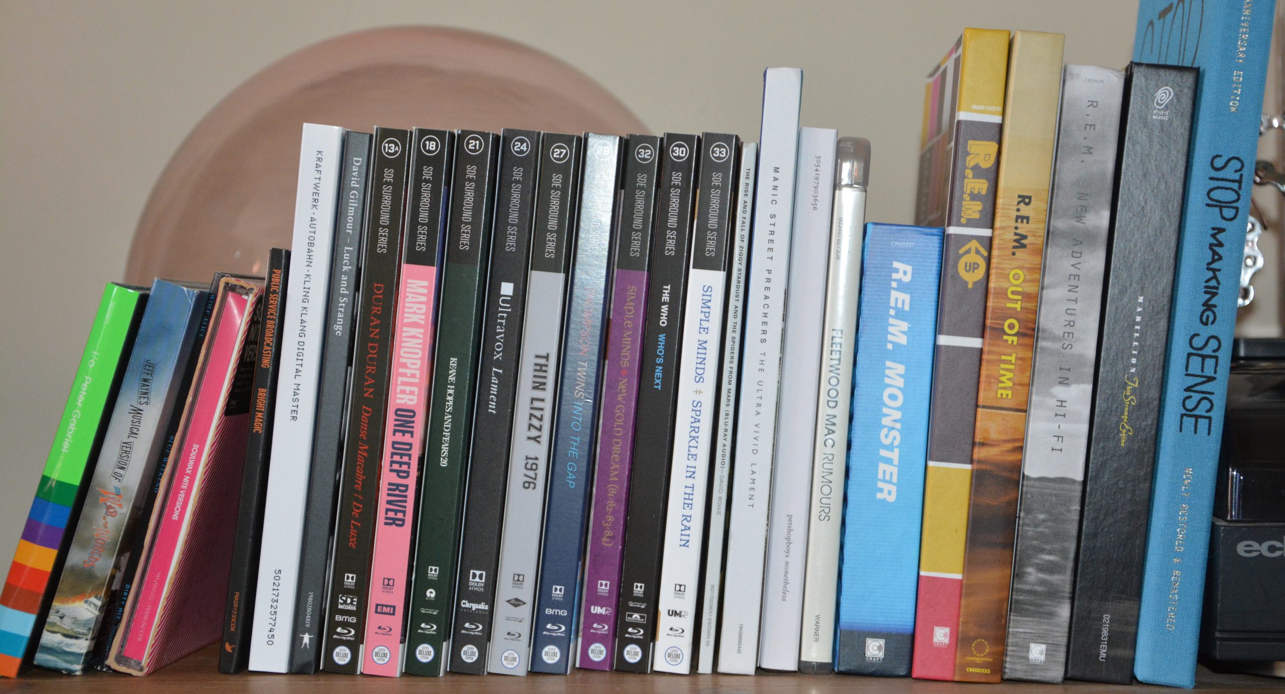 A neatly organized shelf displays a variety of CD cases, featuring album titles like "Mark Knopfler," "Simple Minds," and "R.E.M." Each case stands upright in a precise row, as if awaiting a team meeting led by Nick Midgley himself.