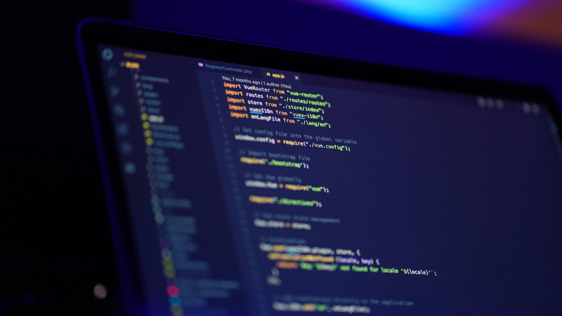 A computer screen displays a code editor with colorful syntax highlighting, showing lines of JavaScript or TypeScript code. The background is dark, with a blue and purple gradient lighting above.